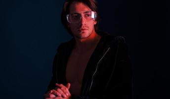 lindo homem gostoso de cabelos compridos em óculos está no estúdio com iluminação neon azul foto
