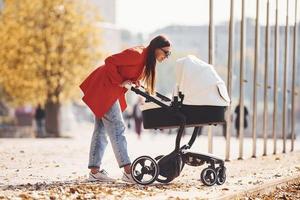 mãe de casaco vermelho dá um passeio com seu filho no carrinho no parque no outono foto