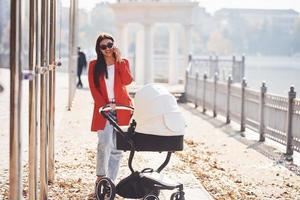 mãe de casaco vermelho dá um passeio com seu filho no carrinho no parque no outono foto
