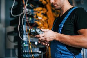 jovem de uniforme tem um emprego com equipamentos de internet e fios na sala do servidor foto