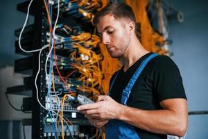 jovem de uniforme tem um emprego com equipamentos de internet e fios na sala do servidor foto