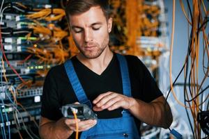 jovem de uniforme tem um emprego com equipamentos de internet e fios na sala do servidor foto