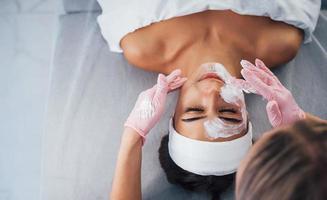 visão aproximada da mulher que está deitada no salão spa e tem procedimento de limpeza facial pela máscara foto
