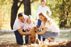família jovem e alegre com cachorro descansa em um parque de outono juntos foto