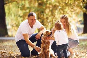 família jovem e alegre com cachorro descansa em um parque de outono juntos foto