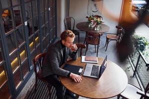 vista superior do jovem elegante com roupa formal que se senta no café com seu laptop foto