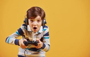 menino bonitinho jogando videogame no estúdio contra fundo amarelo foto