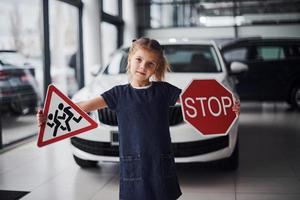 retrato de menina bonitinha que segura sinais de trânsito nas mãos no salão do automóvel foto