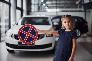 retrato de uma menina bonitinha que segura sinal de estrada nas mãos no salão do automóvel foto