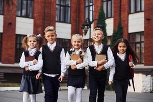 grupo de crianças em uniforme escolar que está ao ar livre perto do prédio da educação foto