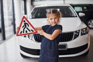 retrato de uma menina bonitinha que segura sinal de estrada nas mãos no salão do automóvel foto