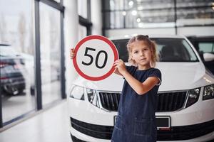 retrato de uma menina bonitinha que segura sinal de estrada nas mãos no salão do automóvel foto