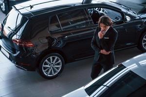 retrato de um jovem empresário bonito de terno preto e gravata dentro de casa perto de carro moderno foto