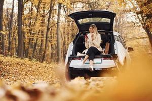 menina senta-se na parte de trás do carro. automóvel novo e moderno na floresta foto