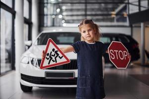 retrato de menina bonitinha que segura sinais de trânsito nas mãos no salão do automóvel foto