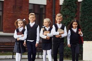 grupo de crianças em uniforme escolar que está ao ar livre perto do prédio da educação foto