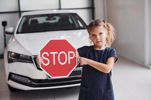 retrato de uma menina bonitinha que segura sinal de estrada nas mãos no salão do automóvel foto