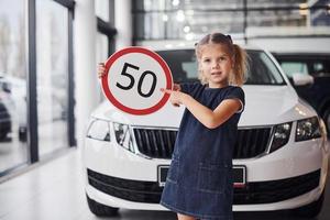 retrato de uma menina bonitinha que segura sinal de estrada nas mãos no salão do automóvel foto