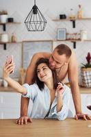 casal juntos na cozinha no horário da manhã com telefone celular foto