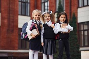 grupo de crianças do sexo feminino em uniforme escolar que está ao ar livre perto do prédio da educação foto