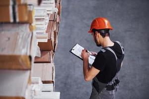 trabalhador de armazenamento de uniforme e bloco de notas nas mãos verifica a produção foto