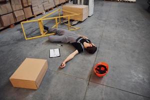 trabalhador do armazém após um acidente no armazenamento. homem de uniforme deitado no chão foto