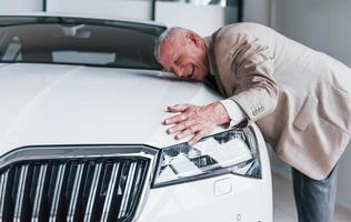 homem envelhecido alegre com roupa formal fica na frente do carro branco moderno foto