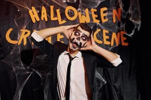 retrato do homem que está na festa temática de halloween em maquiagem de esqueleto assustador e fantasia contra a parede da cena do crime foto
