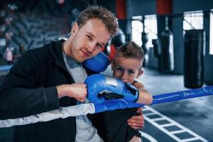 retrato do jovem treinador com garotinho de pé no ringue de boxe foto