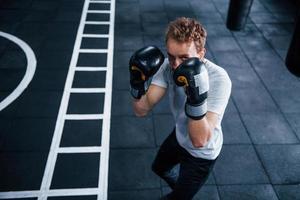 jovem de camisa branca e luvas de proteção de boxe fazendo exercícios no ginásio foto