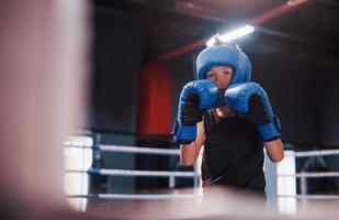 menino em equipamento de proteção esportivo em pé no ringue de boxe e fazendo exercícios foto