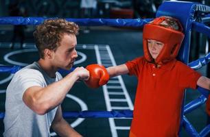 jovem treinador de boxe está ajudando o menino em roupas de proteção no ringue entre as rodadas foto