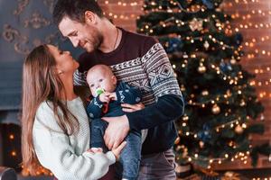 pai e mãe com seu filho juntos no quarto decorado de natal foto