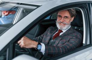 feliz elegante homem sênior com cabelos grisalhos e bigode está no carro moderno foto
