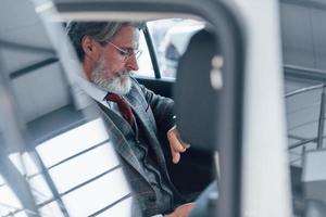 homem sênior elegante moderno com cabelos grisalhos e bigode olha para seus relógios dentro do automóvel foto