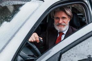 feliz elegante homem sênior com cabelos grisalhos e bigode está no carro moderno foto