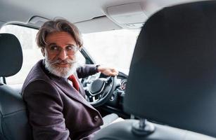 homem sênior elegante moderno com cabelos grisalhos e bigode está no carro moderno foto