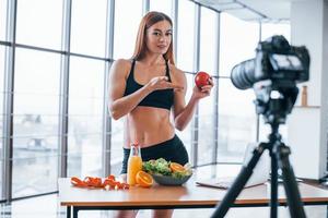 vlogger feminina com corpo esportivo em pé dentro de casa perto da mesa com comida saudável foto