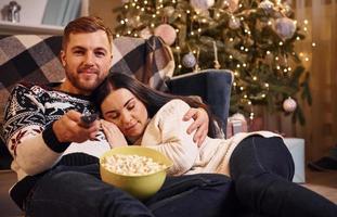 jovem casal dentro de casa no quarto decorado de natal sentado no chão e comemorando o ano novo foto