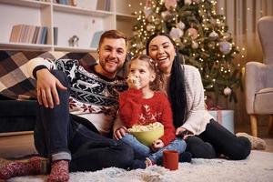 família feliz dentro de casa no quarto decorado de natal comemorando o ano novo com pipoca foto