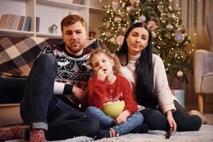 família feliz dentro de casa no quarto decorado de natal comemorando o ano novo com pipoca foto