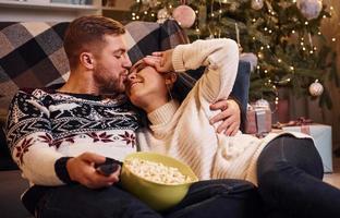 jovem casal dentro de casa no quarto decorado de natal sentado no chão e comemorando o ano novo foto