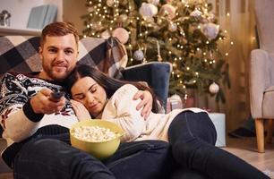 jovem casal dentro de casa no quarto decorado de natal sentado no chão e comemorando o ano novo foto