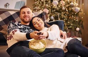 jovem casal se abraçando dentro de casa no quarto decorado de natal foto