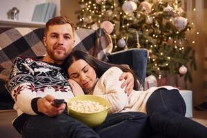 jovem casal dentro de casa no quarto decorado de natal sentado no chão e comemorando o ano novo foto