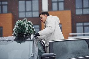 homem de roupa branca colocando pinheiro de natal em cima do carro ao ar livre foto