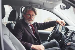 homem sênior na moda em roupas elegantes está no carro moderno foto