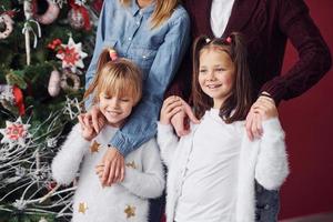 duas meninas ficam juntas com a mãe e o pai no quarto com árvore de natal foto