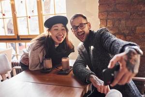 casal multirracial fazendo selfie no café. menina asiática com seu namorado caucasiano foto