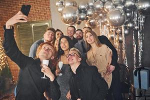 homem tirando selfie de seus amigos que estão na sala decorada de natal e comemorando feriados de ano novo foto